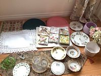 Wide view of all items including placemats, napkins, serving tray, cream and sugar set, plant pots, faux flowers, porcelain plates and bowls