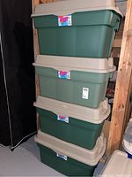 Four stacked Rubbermaid 30 gallon Rough Tote storage boxes with beige hinged lids, in basement storage space.