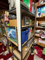 Side view of metal shelf showing four shelves with some items stored for size reference. Shelf frame is grey metal with particle board shelves with visible wear.