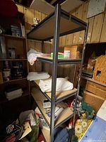 Side view of metal shelf with four particle board shelves, items on shelves, wood paneled walls in background.