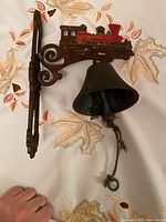 Full view of cast iron bell mounted on bracket with red steam locomotive train decoration.