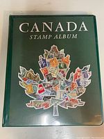 Green hardcover album titled 'Canada Stamp Album' with a maple leaf logo composed of Canadian stamps on front cover