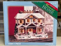 Front of original packaging showing the lit Christmas house decoration and branding
