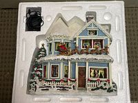 Top-down photo of the lighted ceramic Christmas house decoration secured in original Styrofoam packaging with electrical cord attached.
