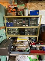 Wide view of metal shelving unit with multiple plastic drawer organizers and various papers and small parts below