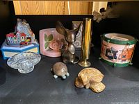 Top view of lot with musical house, pink planter, brass vase, glass ashtray, metal drum, and carved stone turtles.
