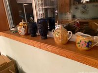 Photo showing all items in the lot arranged on a windowsill: teapot, two ceramic pitchers, and six blue glass cups.