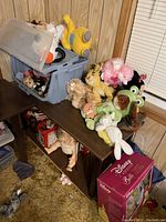 Photo showing various vintage stuffed animals, including Simba, a frog, a pink poodle, and others on a shelf along with a Disney Barbie box on floor.