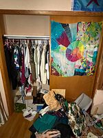 Full view of a closet with hanging vintage women's clothing and some folded clothes and boxes on the floor.