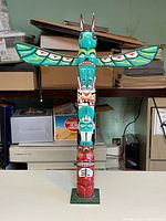 Frontal view of the hand-painted miniature wooden totem pole showing detailed face and animal motifs with wings extended.