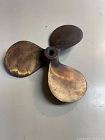 Top-down view of a three-blade metal propeller showing curved blades and hexagonal central mount.