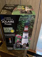 Box of Moonrays solar powered lighthouse garden ornament showing French and English text and product image.