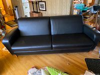 Full front view of black leather couch with two seat cushions on hardwood floor