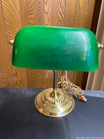 Front view of vintage bankers lamp showing green glass shade and brass base with power cord.