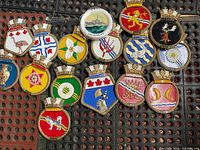 Top-down view of the 15 decorated vintage metal plaques featuring various crests, symbols, flowers, animals, and regions.