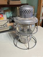 View of the vintage Adlake Kero railroad lantern from one side showing the wire cage, glass globe, and vented top with embossed brand.