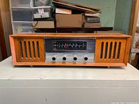 Front view of vintage Strauss radio showing wooden cabinet with vertical speaker grills, analog tuning dial panel and four knobs.