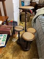 Vintage wooden tiered stand with four cane-topped round platforms on turned wooden legs, seen in room setting on carpet.