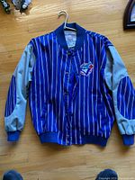 Front view of blue pinstriped jacket with gray sleeves and elbow patches, team logo on chest, hung on a hanger.