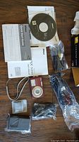 Nikon Coolpix S210 with manual, software CD, cables, battery charger, and camera case laid out flat on wooden surface