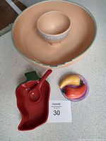 Overall view of large peach chip bowl with smaller dip bowl inside, red chili pepper salsa dish with spoon, and colorful salt and pepper shakers with base.