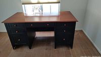 Front view of the desk showing black body, wood top, and multiple drawers with round wood pulls.