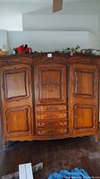 Front view of entire antique wooden armoire showing three doors and four drawers with carved decorative panels.