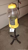 Full view of the gumball machine with iron stand, showing yellow base and top, and clear glass globe.