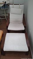 Brown wood IKEA chair with cream cloth cushions and ottoman positioned on floor