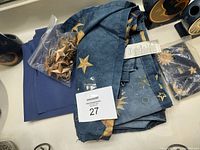 Blue fabric shower curtain and liner with gold star hooks on table, with folded towels and waste can visible