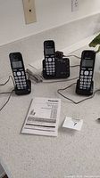Three black Panasonic cordless phones with cords on a white countertop, including a main base station with answering machine and two charging bases.
