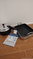 Mirro pressure cooker, Emil's Chef aluminum roasting pan with rack and recipe instruction book on brown floor