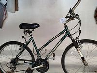 Full side view of a dark green women's mountain bike showing frame, wheels, seat, pedals, and handlebars.