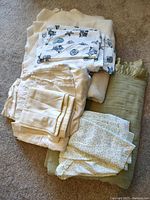 Five bedding items folded on carpet: three sheet sets and two blankets. One sheet set with ocean motif in blue and white visible on top.