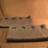 Two beige blackout curtain panels folded showing metal grommets and textured fabric.