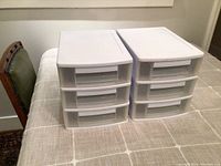 Two stacked white plastic organizers with three drawers each on a table, lit from above showing front and top views.