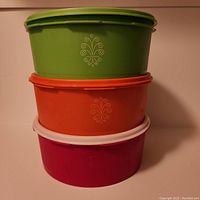 Stacked view of three vintage Tupperware Servalier cookie canisters. Red bottom, orange middle, green top. Each has decorative mid-century modern logo on the side.