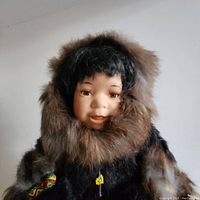Close-up of the porcelain doll's face and fur-trimmed parka hood showing facial features and fur texture.
