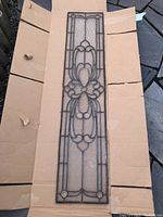 Full view of antique leaded glass panel laid on cardboard, showing entire length and design.