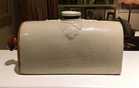 Full side view of rectangular stoneware bed foot warmer with screw top lid and wooden handle, showing decorative molded detail.