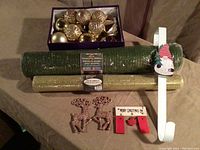 Photo showing green and gold mesh ribbons, box of gold and bronze Christmas ornaments, and white over-the-door Santa wreath hanger