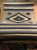 Full view of the blanket showing the central large diamond pattern with surrounding smaller geometric motifs and horizontal stripes in blues, black, cream, and gray.