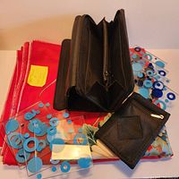 Photo showing the fabric folded with two wallets on top and a stack of eight patterned glass tiles/coasters arranged in front.
