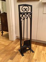Full view of black metal stand holding four fireplace tools on hardwood floor.