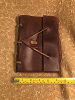Front of leather bound journal with leather string tie closure and measuring tape showing approximately 5.5 inches width