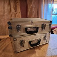 Two stacked vintage silver metal cases with black handles and metal locking latches, branded Optex.