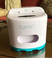 Full view of white and teal Lumin CPAP sanitizer device on glass table showing front side with brand name and power button on top.