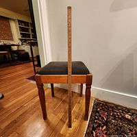 Photo showing the Singer sewing stool with dark cushioned seat and wood yardstick standing vertically next to it for scale, on wooden floor background