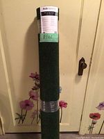 Rolled dark green rug with label attached at the top and middle, showing it is new and sealed.