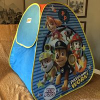 Front side of the blue fabric play tent with Paw Patrol character print and yellow trim.